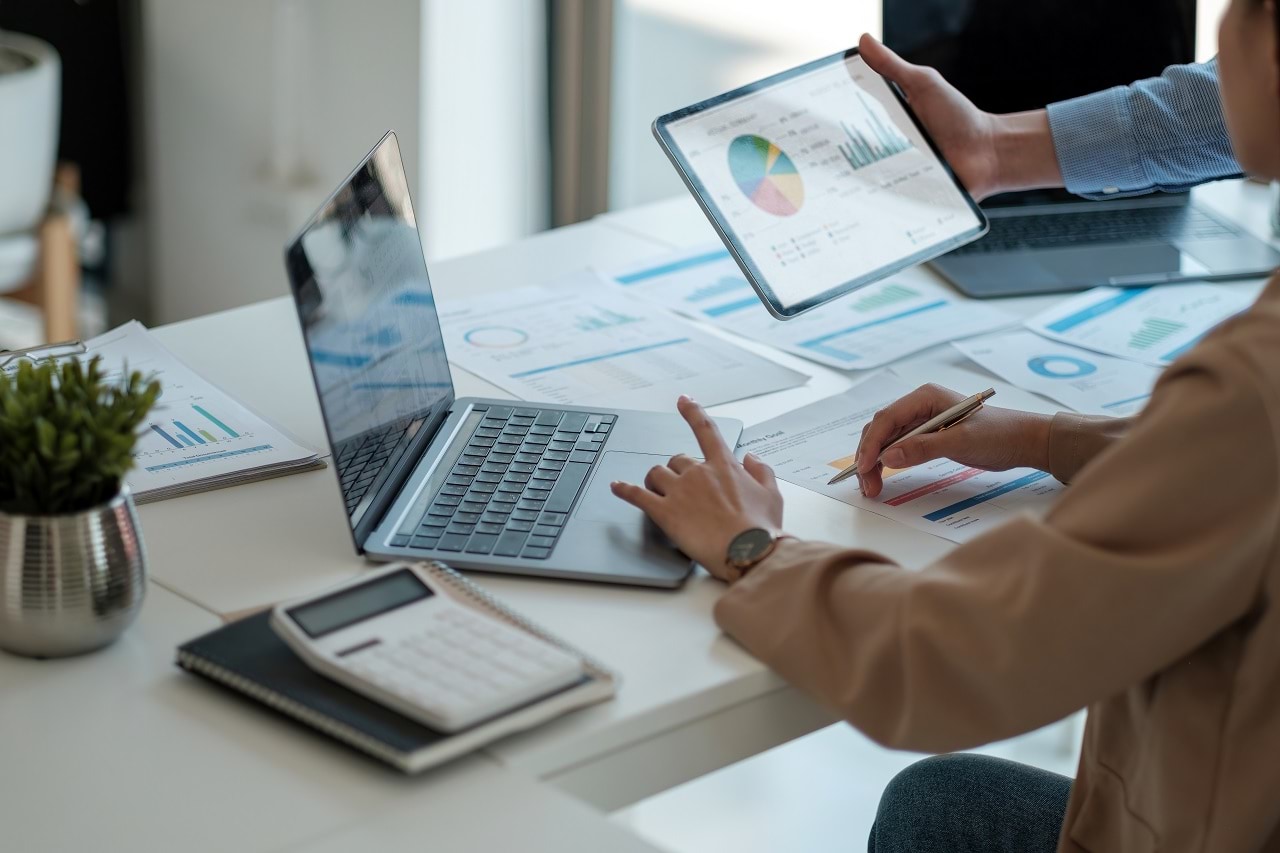 Image of a desk with two co-workers using technology to work together. 